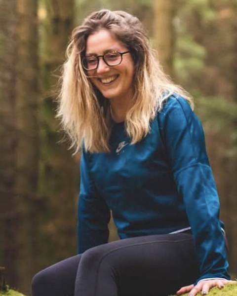 Carly smiling, sitting on a mossy log in a forest