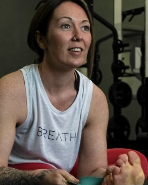 Laura sitting on a yoga mat with a strap round her foot